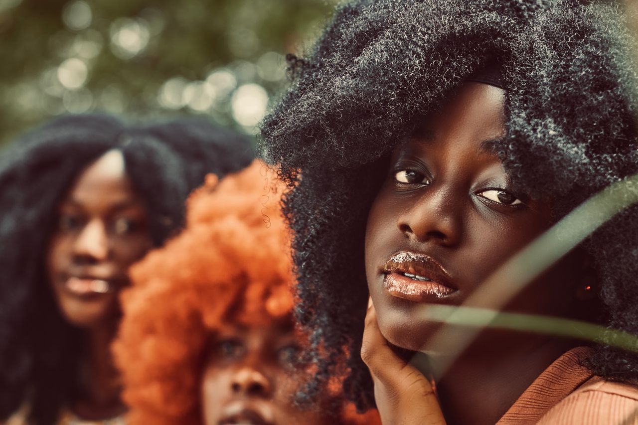 Close-up portrait of three black women showcasing diverse natural hairstyles in warm tones.